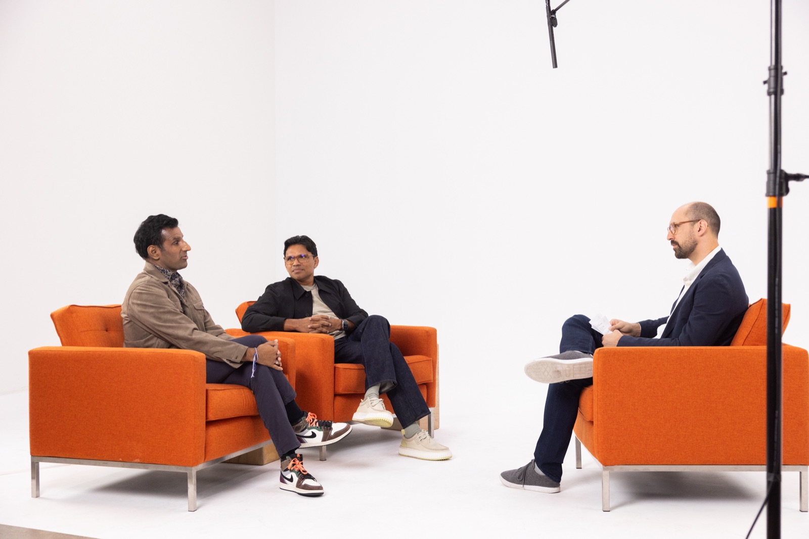 Josh interviewing Nick Mehta and Chuck Ganapathi on orange armchairs in a white studio